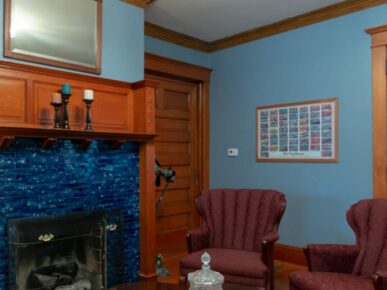 The main parlor has a fireplace and two red chairs with fine crystal on the table